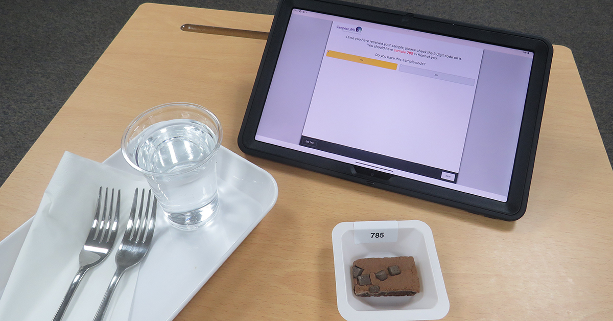 Consumer test setup with chocolate brownie, electronic tablet and water on desk